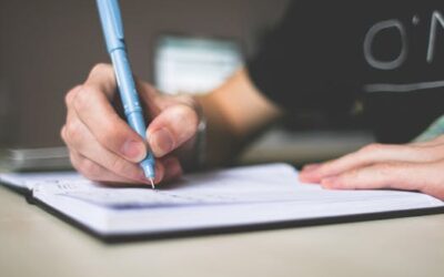Close-up of hand writing in notebook using a blue pen, focus on creativity.